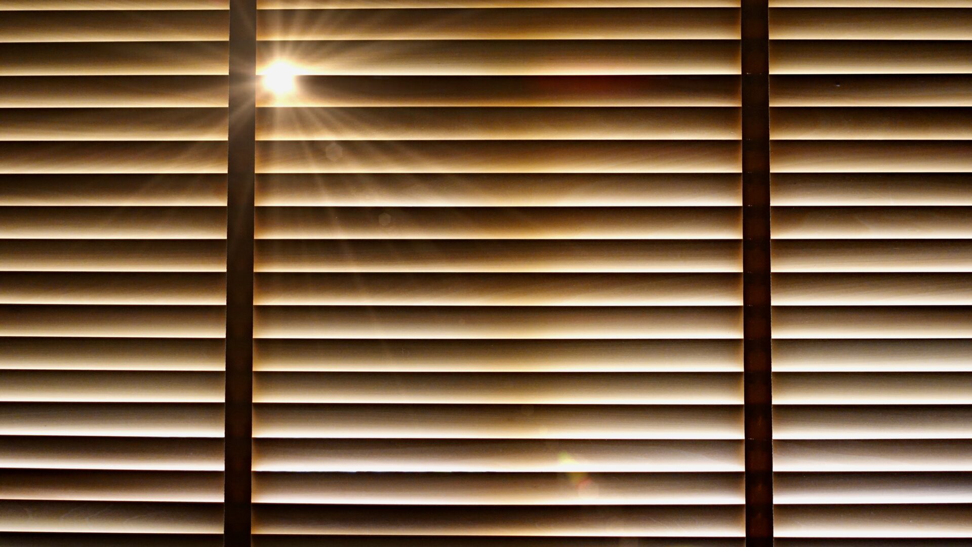 Closed wooden blinds with the evening sun light outside.
