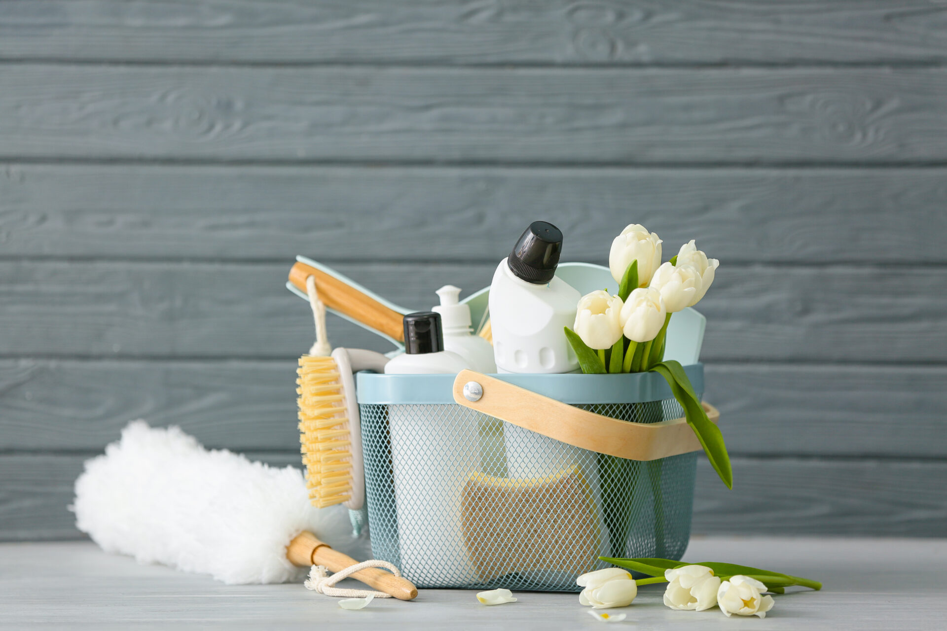 Set of cleaning supplies for roller window shades and spring flowers on grey wooden background. Wholesale Blind Factory