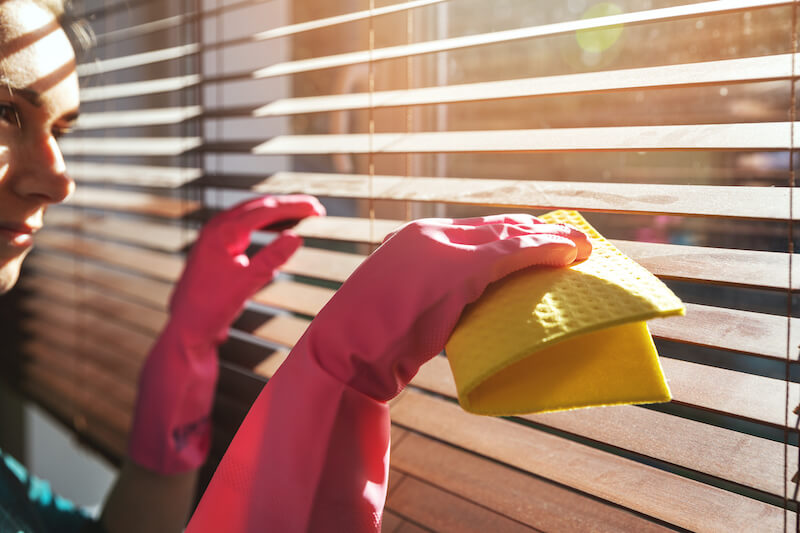 woman showing us how to clean faux wood blinds with pink gloves and yellow damp cloth